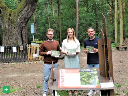 Am Kraftort „De Decke Boom“ in Kreuzau-Stockheim stellen Dennis Winands (Rureifel Tourismus), Lea Schenkelberg und Nicolas Gath (beide Naturpark Nordeifel) die Broschüre mit kurzen Wandertouren zu den 15 Kraftorten vor. (v.l.n.r.) <span class="copy">&copy; Naturpark Nordeifel</span>